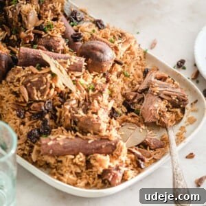 Lamb kabsa served on a white platter with a silver spoon, surrounded by glasses of water and bowls of yogurt.