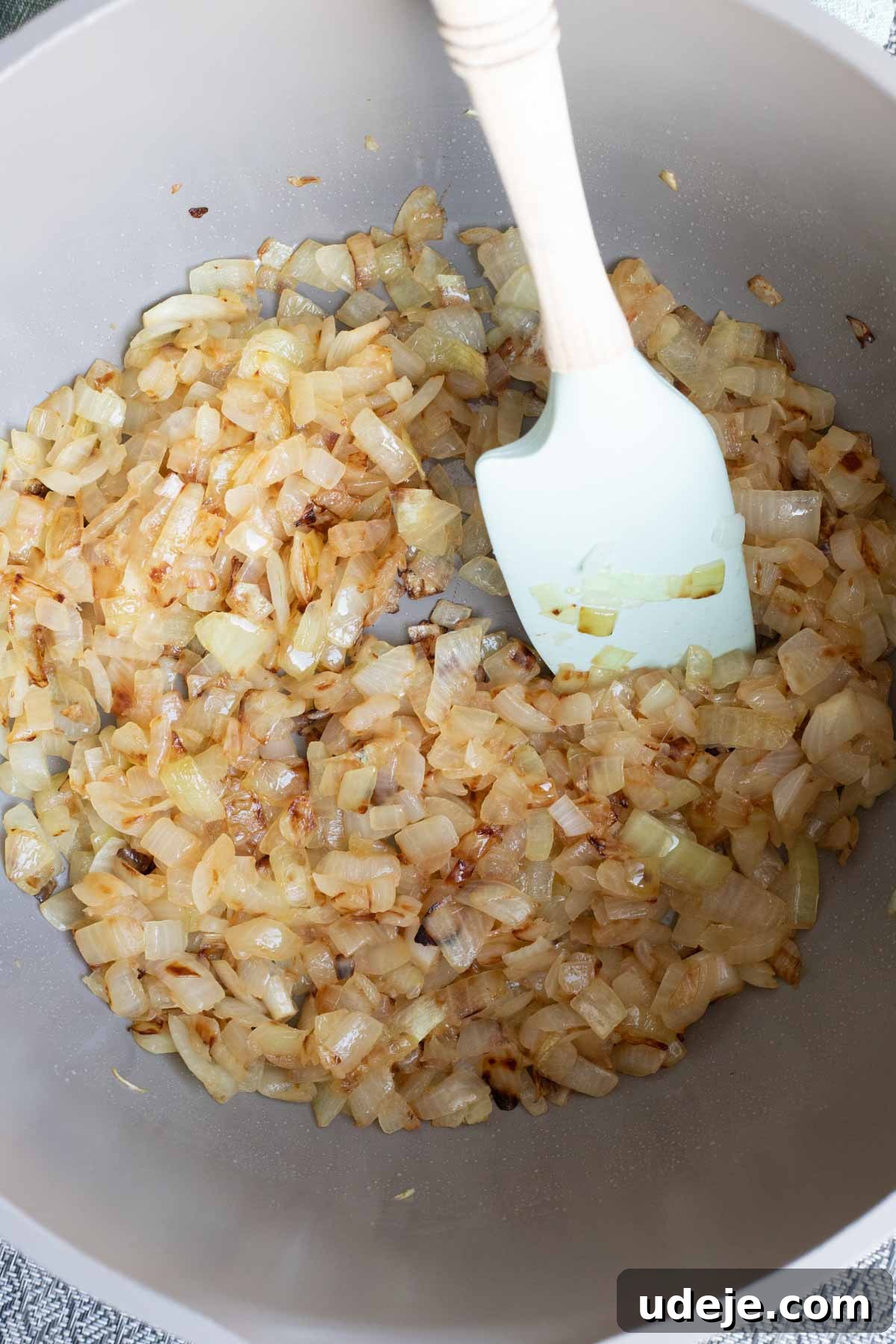 Chef's Signature Lamb Kabsa 5 Diced onions being sautéed to a golden brown in a pot, stirred with a white spatula—the perfect aromatic base for flavorful lamb kabsa.
