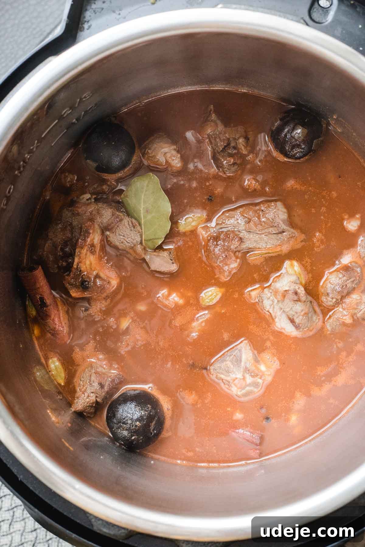 Chef's Signature Lamb Kabsa 8 Chunks of meat, whole spices, and bay leaves simmer in a rich, reddish-brown lamb kabsa stew inside a stainless steel pot. Steam rises from the hot mixture, hinting at slow-cooked tenderness.