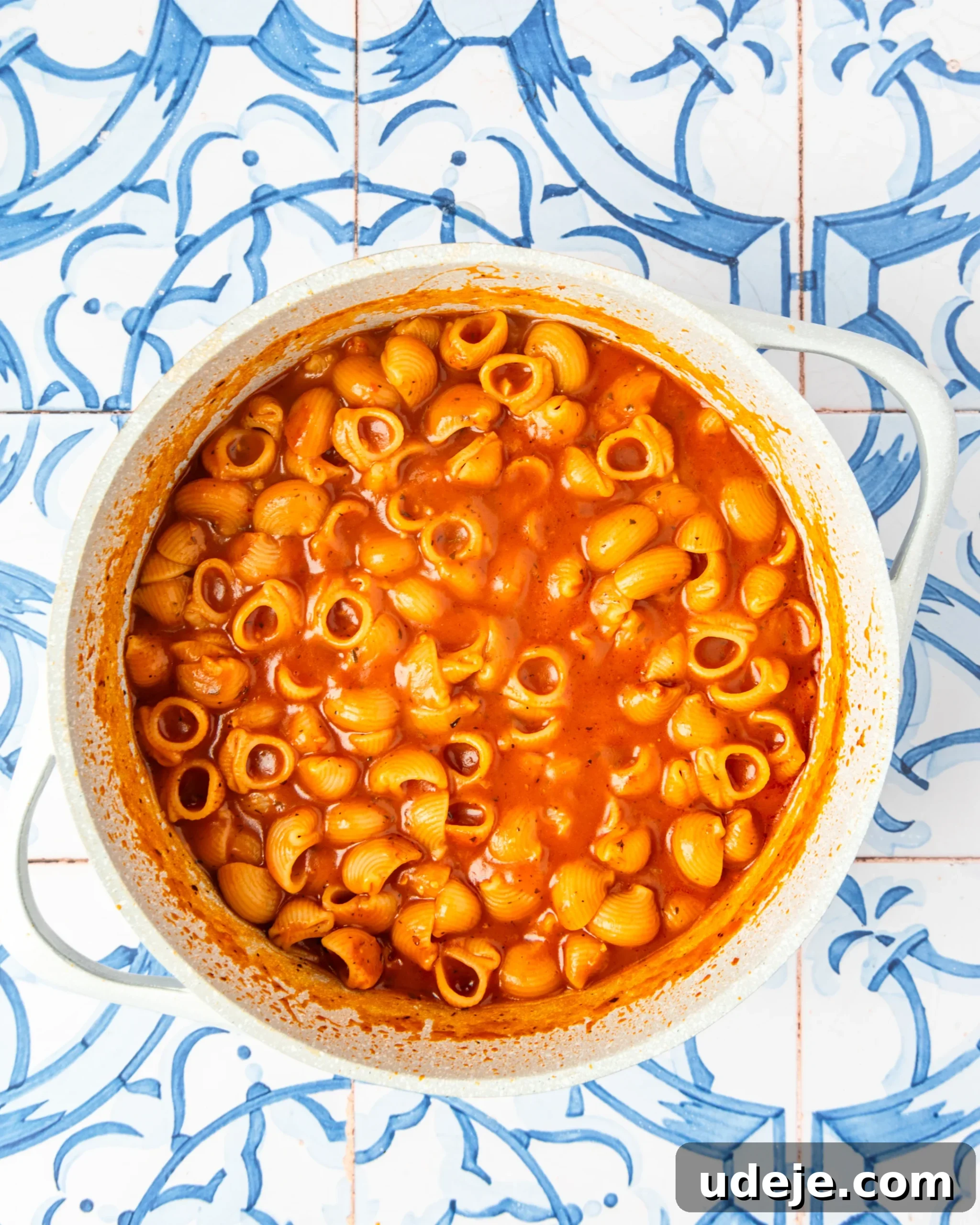 30-Minute One-Pot Creamy Pink Pasta 11 White pot with cooked shell pasta in tomato sauce on a blue and white tiled background.
