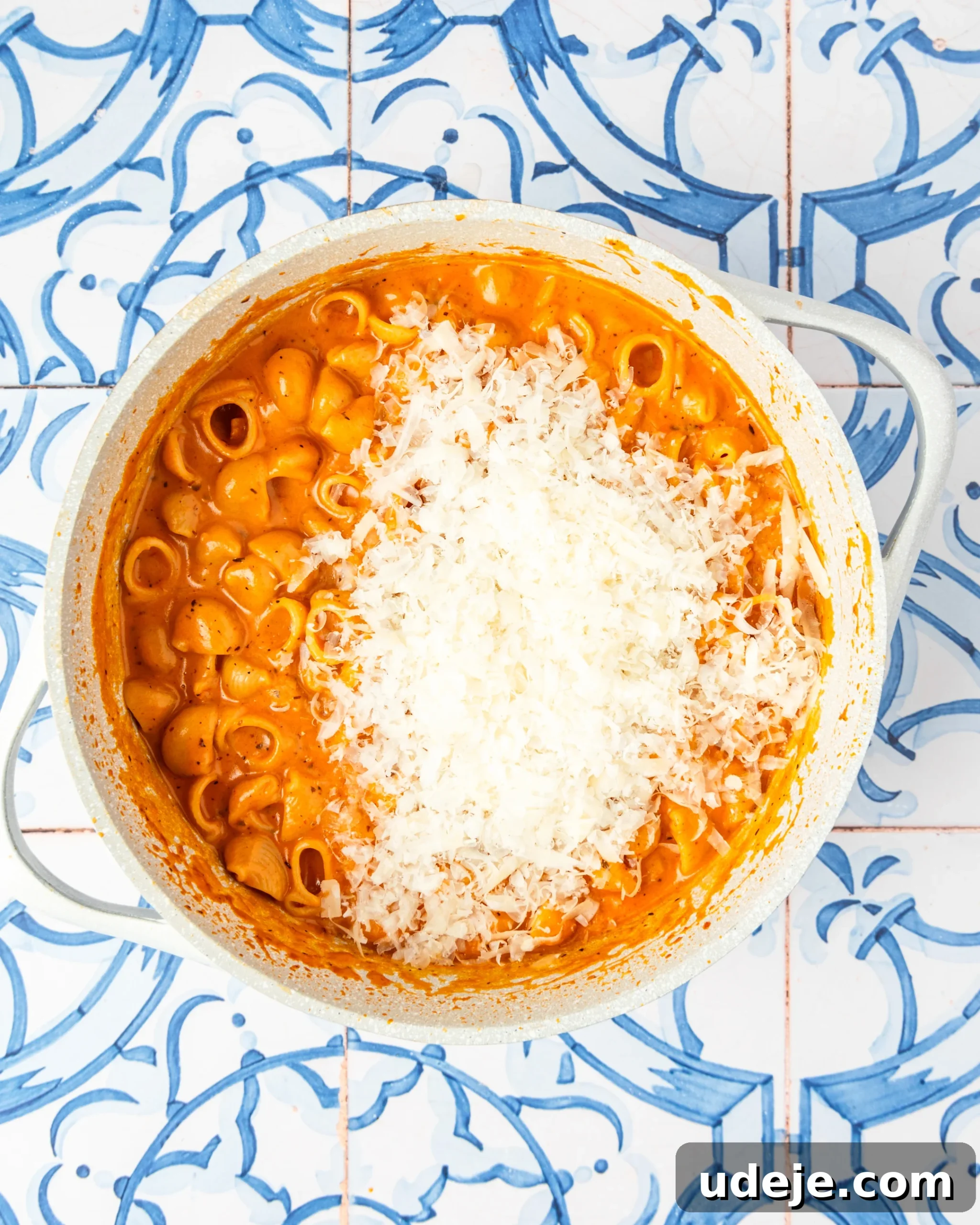 30-Minute One-Pot Creamy Pink Pasta 13 White pot with shell pasta in a light orange sauce and parmesan on top on a blue and white tiled background.