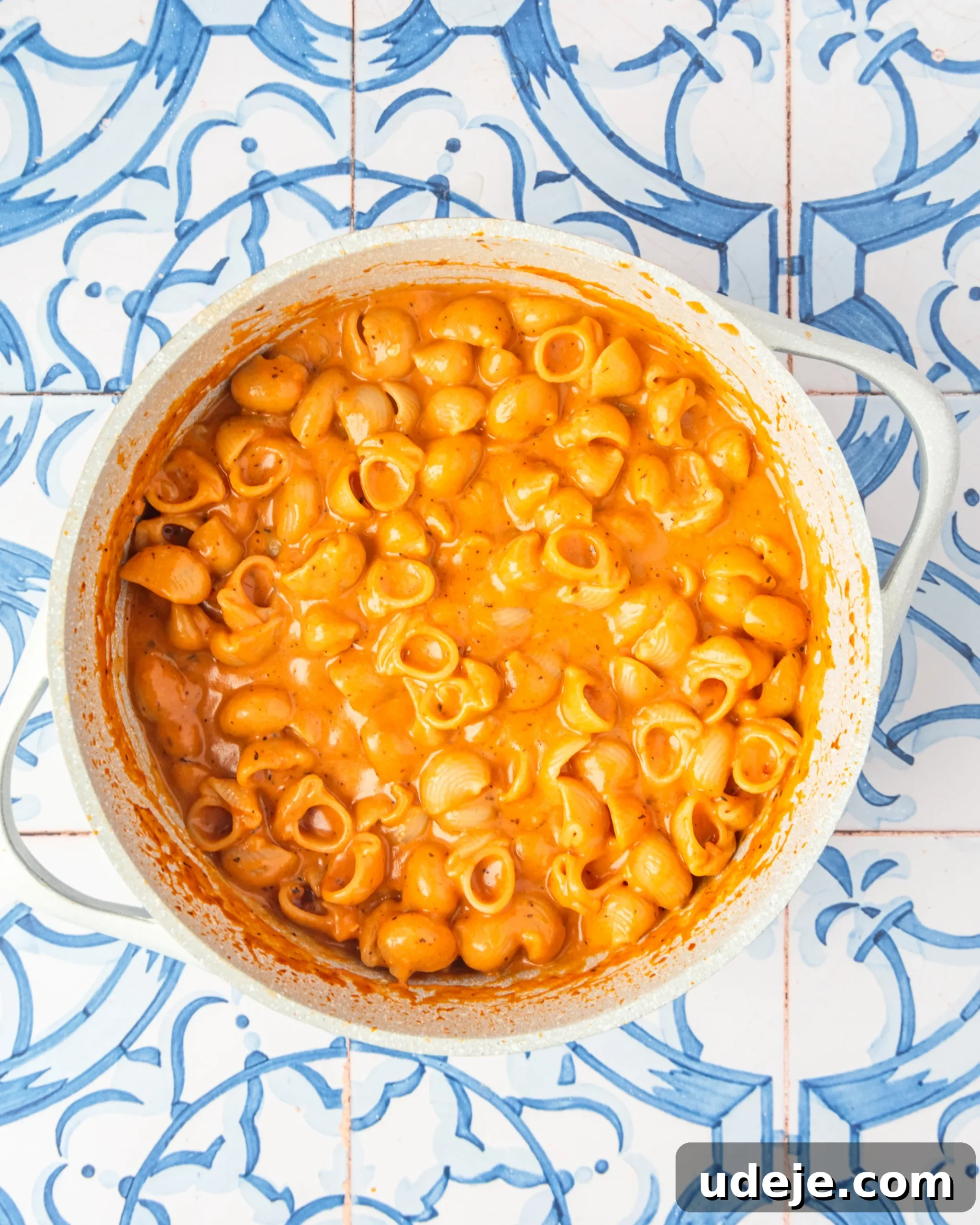 30-Minute One-Pot Creamy Pink Pasta 14 White pot with shell pasta in a light orange sauce on a blue and white tiled background.
