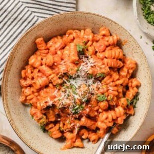 30-Minute One-Pot Creamy Pink Pasta 16 creamy pink sauce pasta in fusili shape is plated in a brown speckled pasta bowl, garnished with parmesan and chopped parsley. It is on a table with a striped napkin, a small parmesan dish, and some parsley in a small dish.