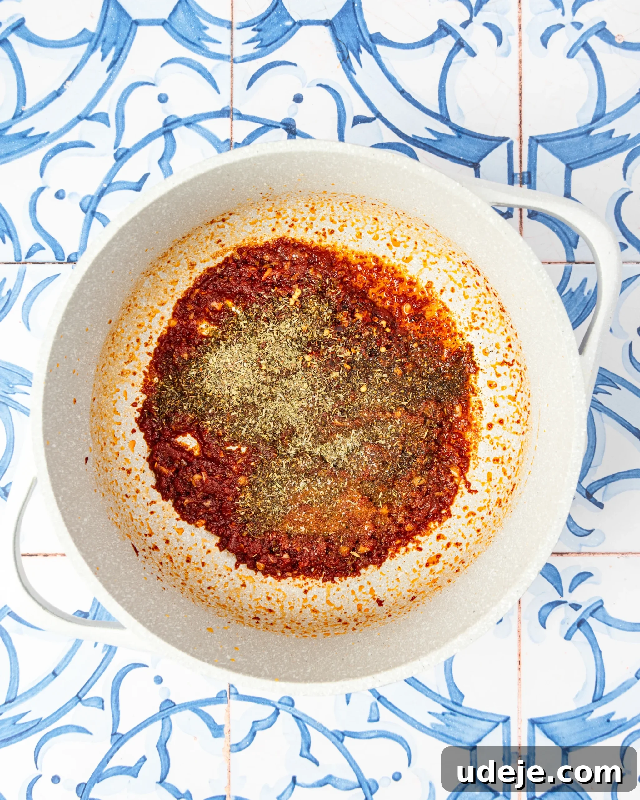 30-Minute One-Pot Creamy Pink Pasta 7 White pot with tomato paste and garlic, and seasonings, cooked on a blue and white tiled background.