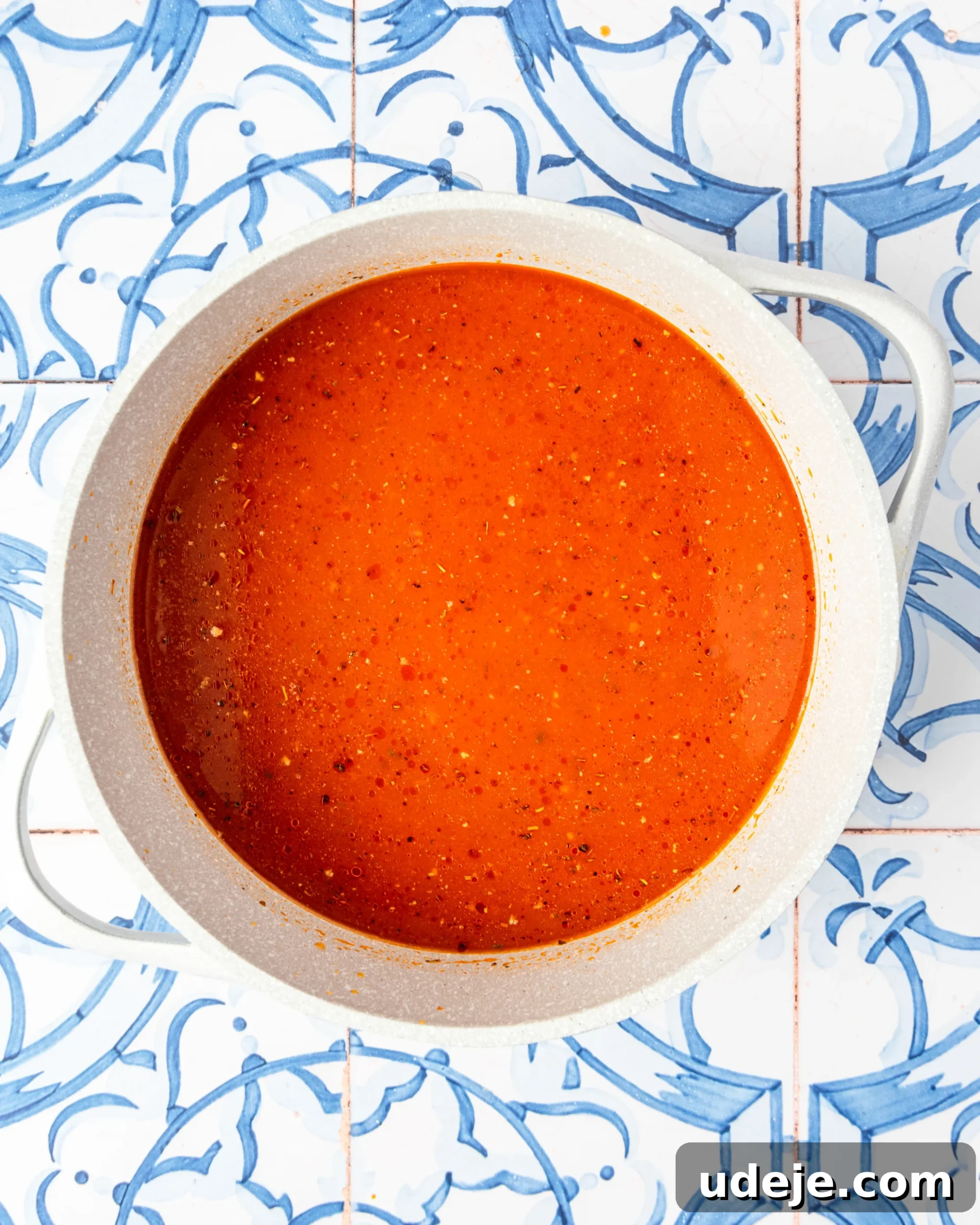 30-Minute One-Pot Creamy Pink Pasta 8 White pot with red liquid and seasonings on a blue and white tiled background.