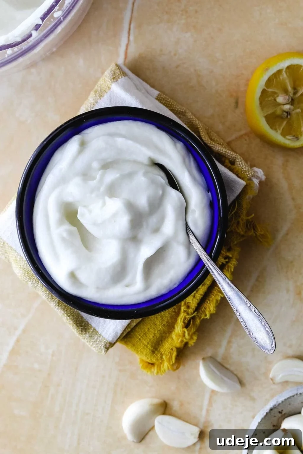 Whip Up Fluffy Toum in 5 Minutes No Food Processor 2 A beautifully presented bowl of creamy white Toum, adorned with fresh parsley, sits ready to be served with warm pita bread. Fresh garlic cloves and a bright lemon add to the vibrant culinary scene.