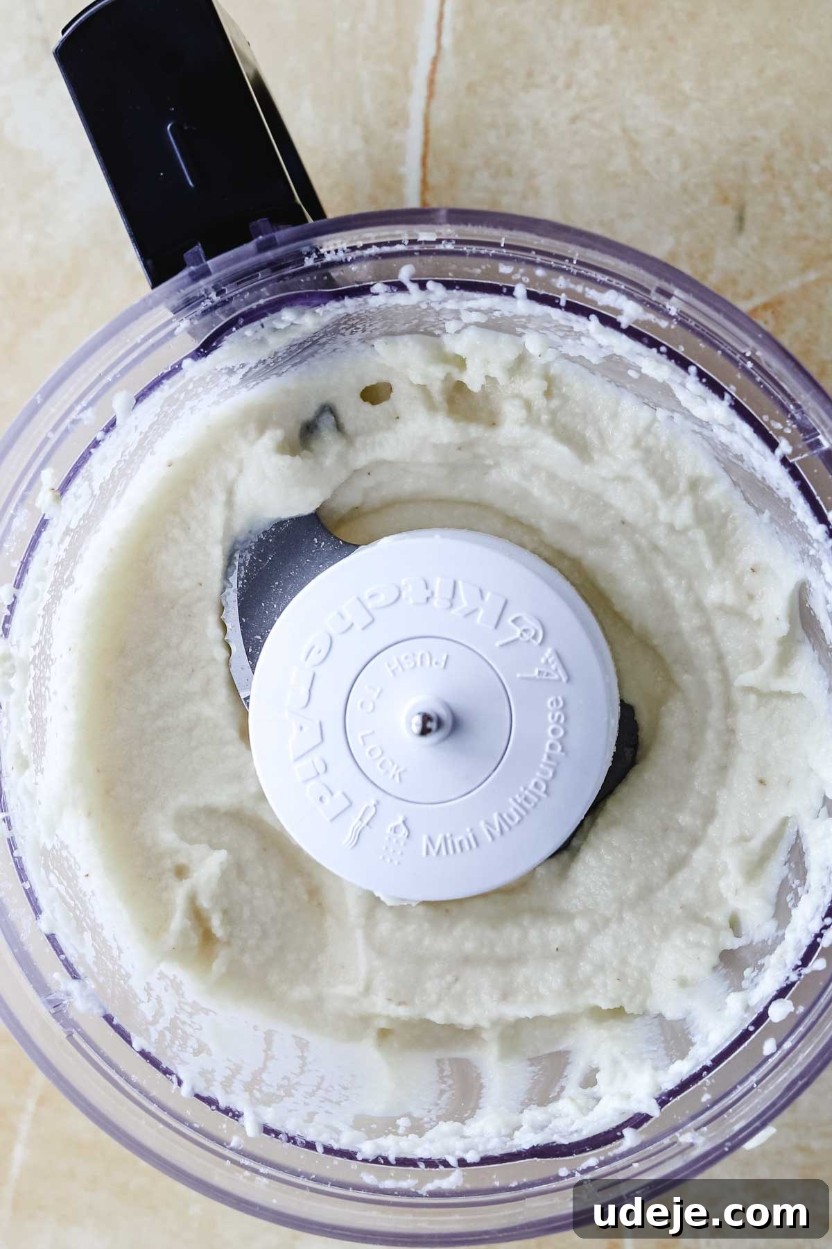 Whip Up Fluffy Toum in 5 Minutes No Food Processor 18 An overhead shot reveals a food processor bowl filled with smooth, creamy Toum, highlighting its rich texture on a light-colored surface.