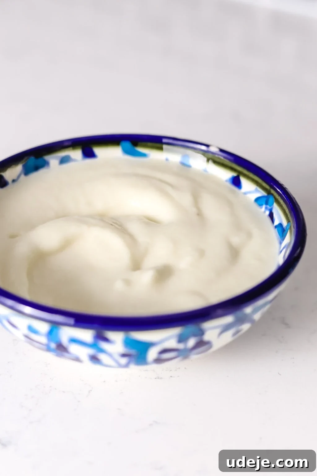 Whip Up Fluffy Toum in 5 Minutes No Food Processor 3 A pristine blue and white ceramic bowl holds a generous portion of smooth, creamy white Toum, resting on a clean white surface, highlighting its enticing texture.