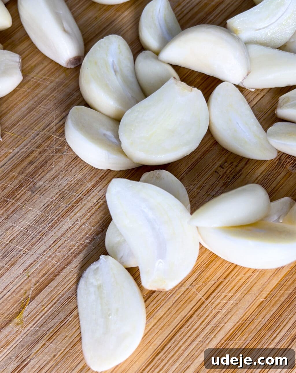 Whip Up Fluffy Toum in 5 Minutes No Food Processor 5 Several pristine peeled garlic cloves are artfully scattered across a rustic wooden cutting board, showcasing their smooth, white surfaces and natural textures, prepared for crafting fresh Toum.