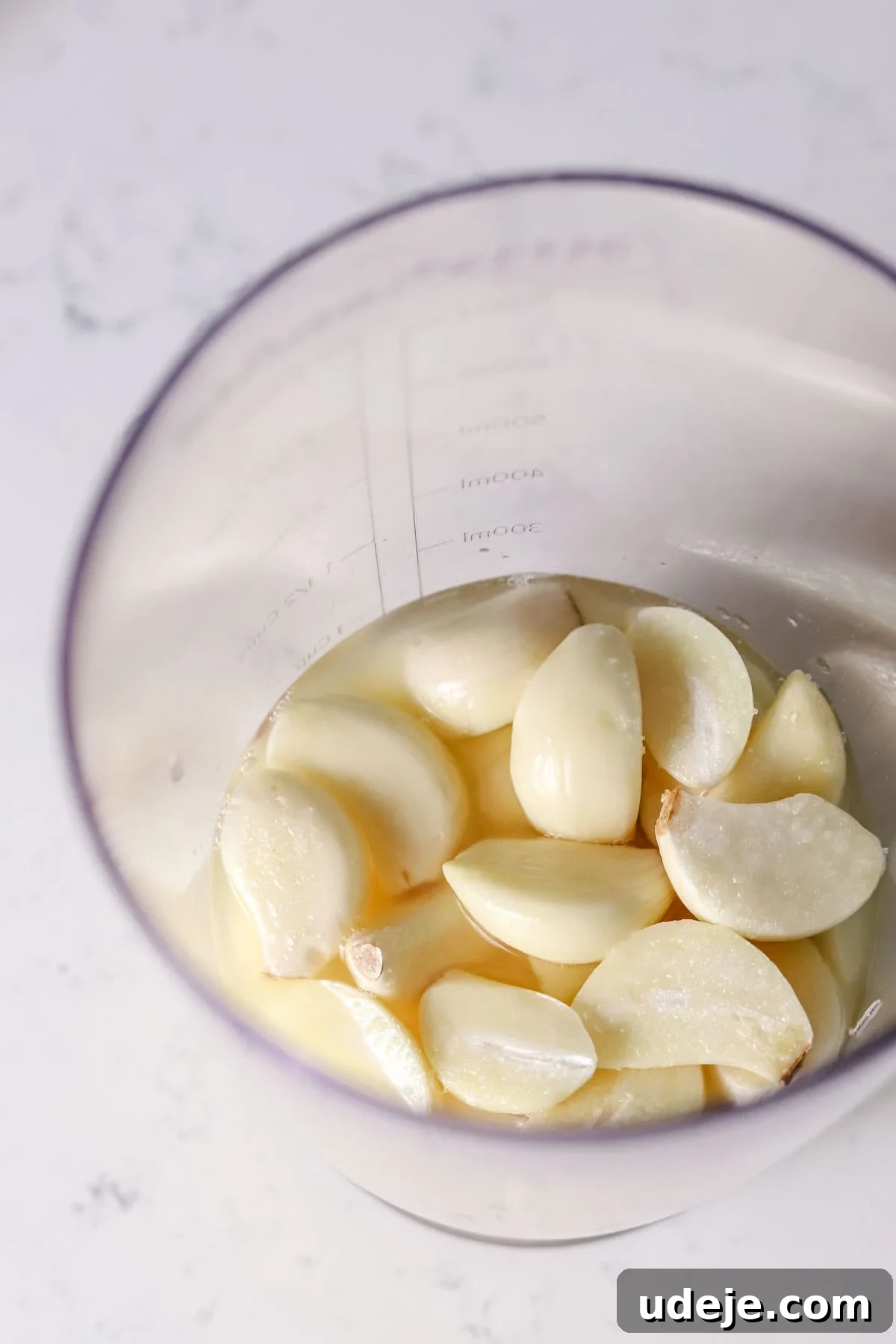 Whip Up Fluffy Toum in 5 Minutes No Food Processor 6 A transparent measuring cup holds a collection of freshly peeled garlic cloves, ready to be transformed into authentic Toum, set on a bright white countertop.