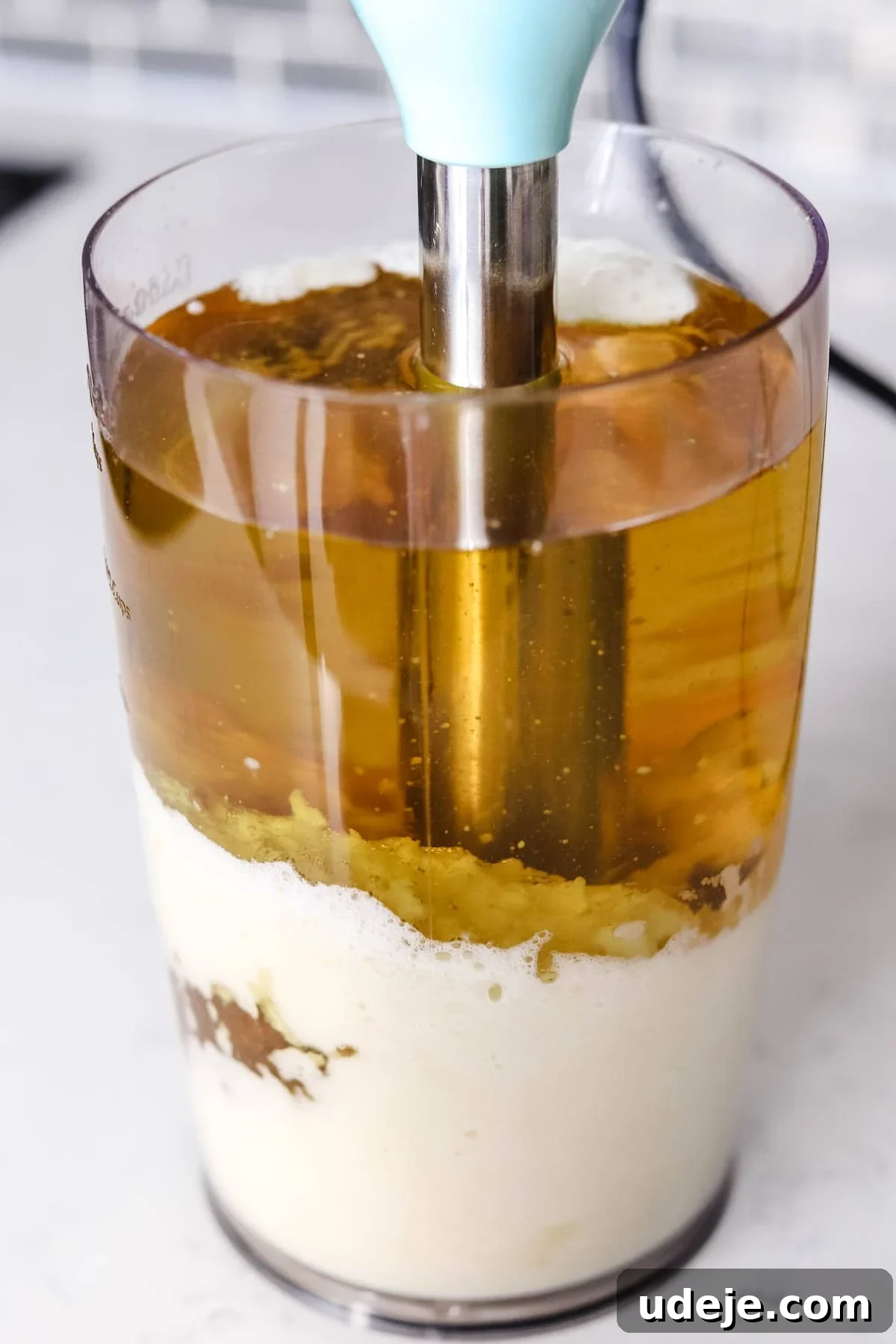 Whip Up Fluffy Toum in 5 Minutes No Food Processor 8 A close-up image showing an immersion blender submerged in a tall, clear container filled with layered ingredients including oil, egg, and mustard, ideal for blending various creamy sauces like mayonnaise or Toum.