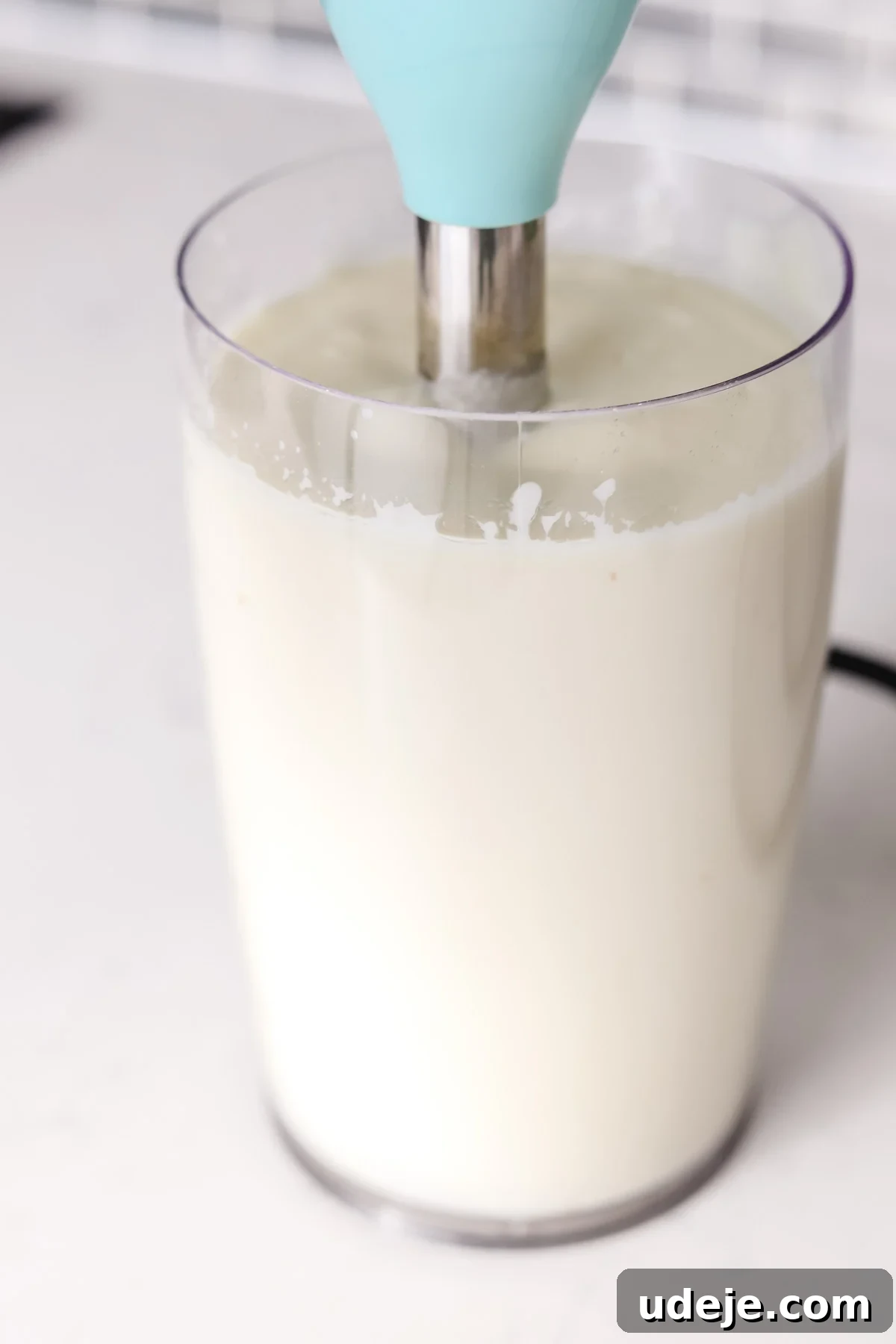 Whip Up Fluffy Toum in 5 Minutes No Food Processor 9 An active hand blender smoothly processes creamy Toum within a tall, transparent container, positioned on a bright countertop, demonstrating the blending phase of the garlic sauce.