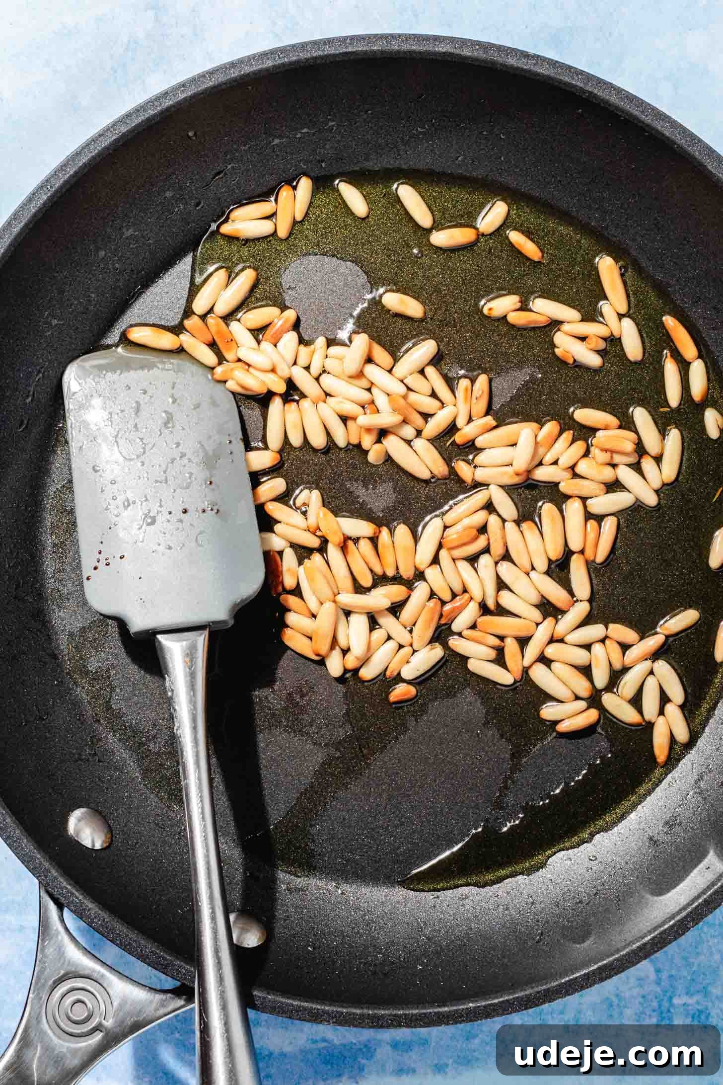 Mediterranean Eggplant Fatteh Delight 9 Pine nuts and olive oil in a small black skillet, with a grey spatula for stirring.