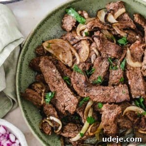 beef shawarma strips served in a green bowl with onion slices and garnished with chopped parsley