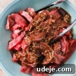 beef shawarma marinating in a blue bowl with a marinade mixture on top and silver tongs