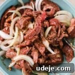 beef shawarma marinating with onions slices in a blue bowl with silver tongs