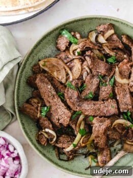 beef shawarma strips served in a green bowl with onion slices and garnished with chopped parsley