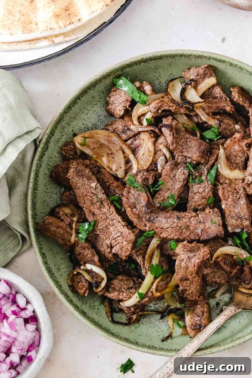 Effortless Skillet Tender Beef Shawarma 9 beef shawarma strips served in a green bowl with onion slices and garnished with chopped parsley