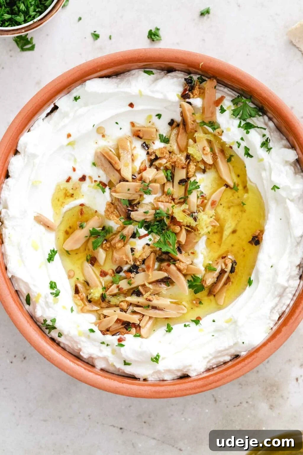 Orange-brown bowl filled with labneh topped with slivered almonds, parsley