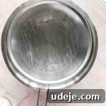 steel bowl with strainer in it, small glass bowl with salt and medium glass bowl with yogurt in top corner, on a pink background
