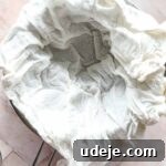 steel bowl with strainer with cheesecloth in the strainer on a pink background