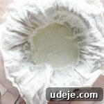 steel bowl with strainer with yogurt in cheesecloth on a pink background