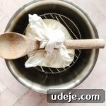 steel bowl with cheesecloth tied to wooden spoon on a trivet, on a pink background