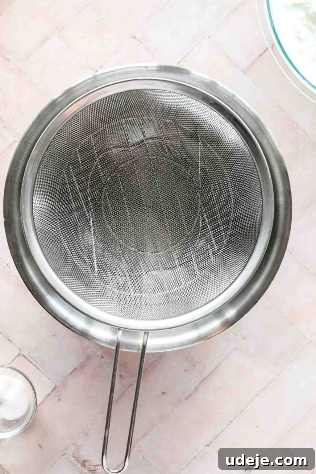 steel bowl with strainer in it, small glass bowl with salt and medium glass bowl with yogurt in top corner, on a pink background