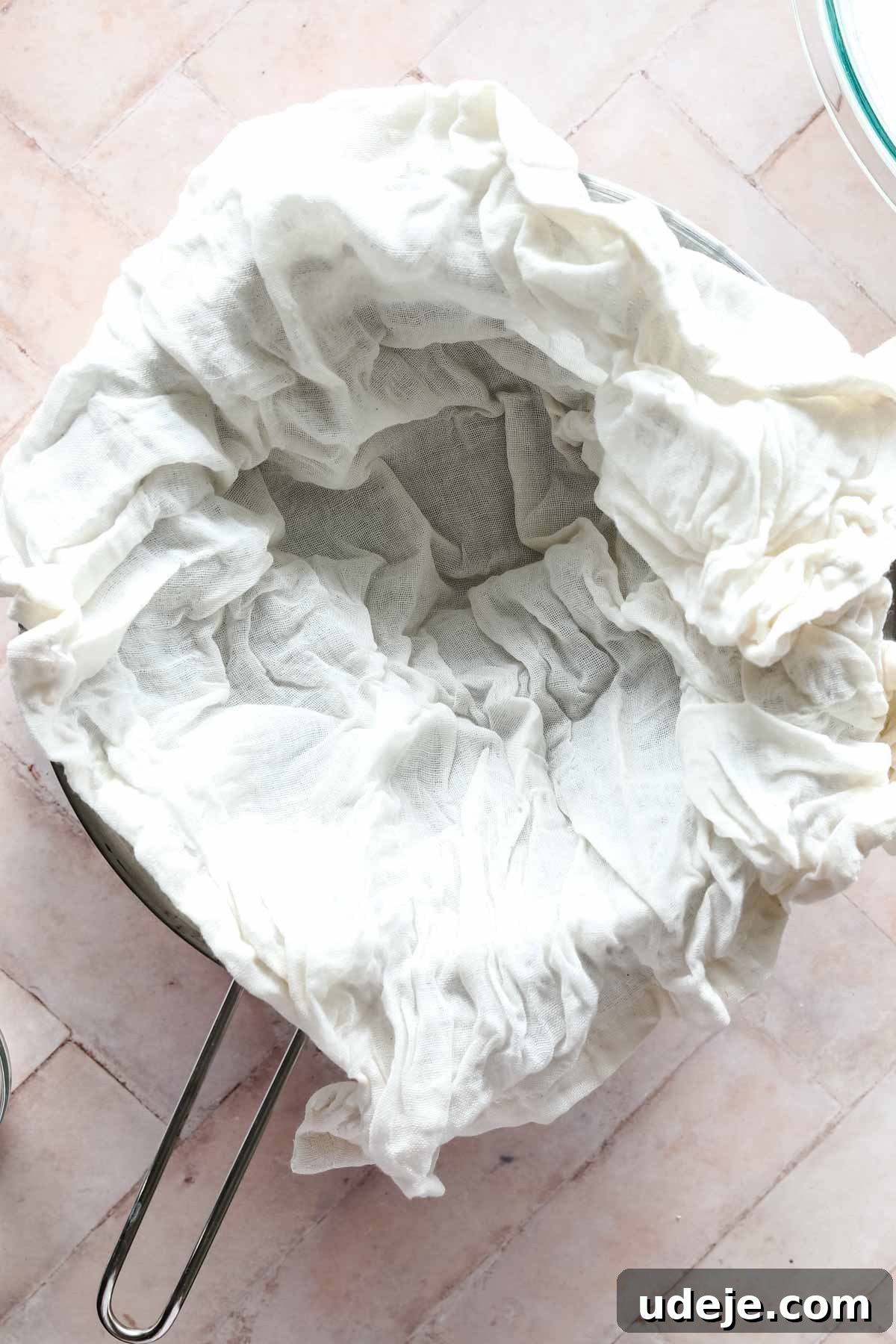 steel bowl with strainer with cheesecloth in the strainer on a pink background