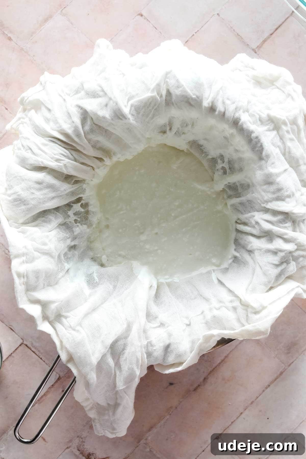 steel bowl with strainer with yogurt in cheesecloth on a pink background