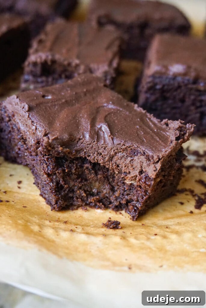 A frosted chocolate snack cake, ready to be sliced, garnished with a few vegan chocolate chips.