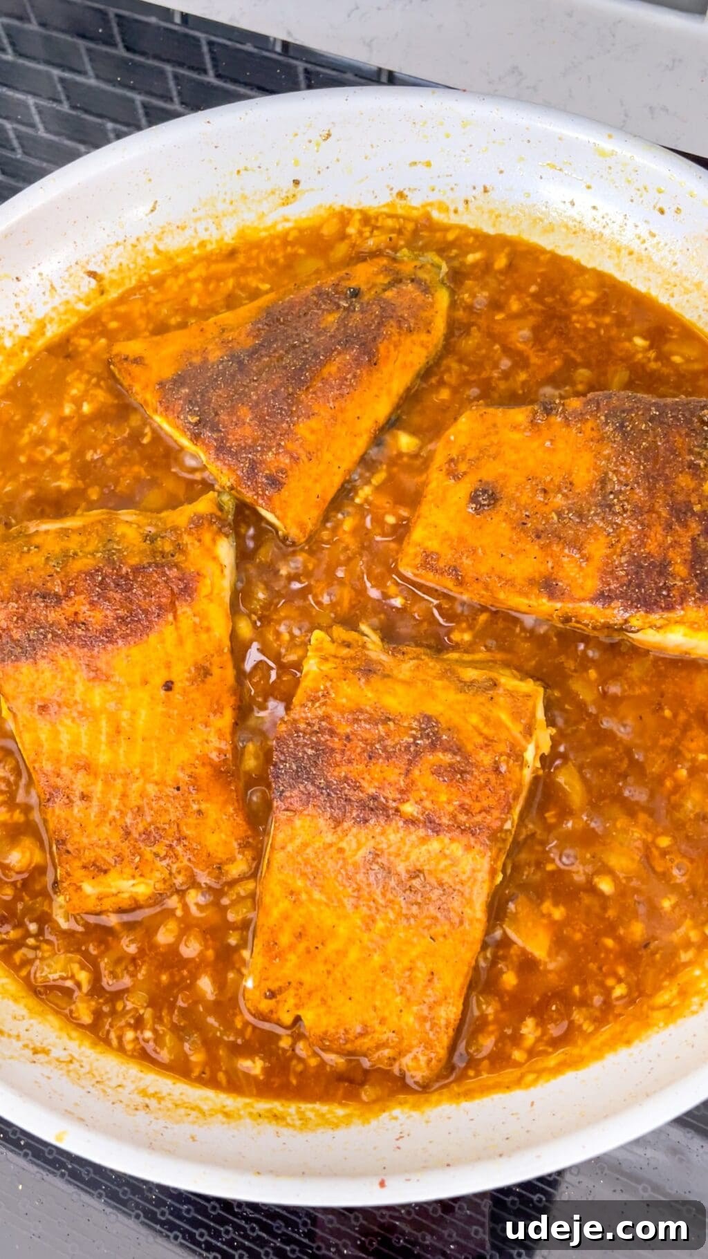 A light-colored skillet showcases perfectly cooked fish pieces nestled in a vibrant and savory tomato sauce, ready to be enjoyed.