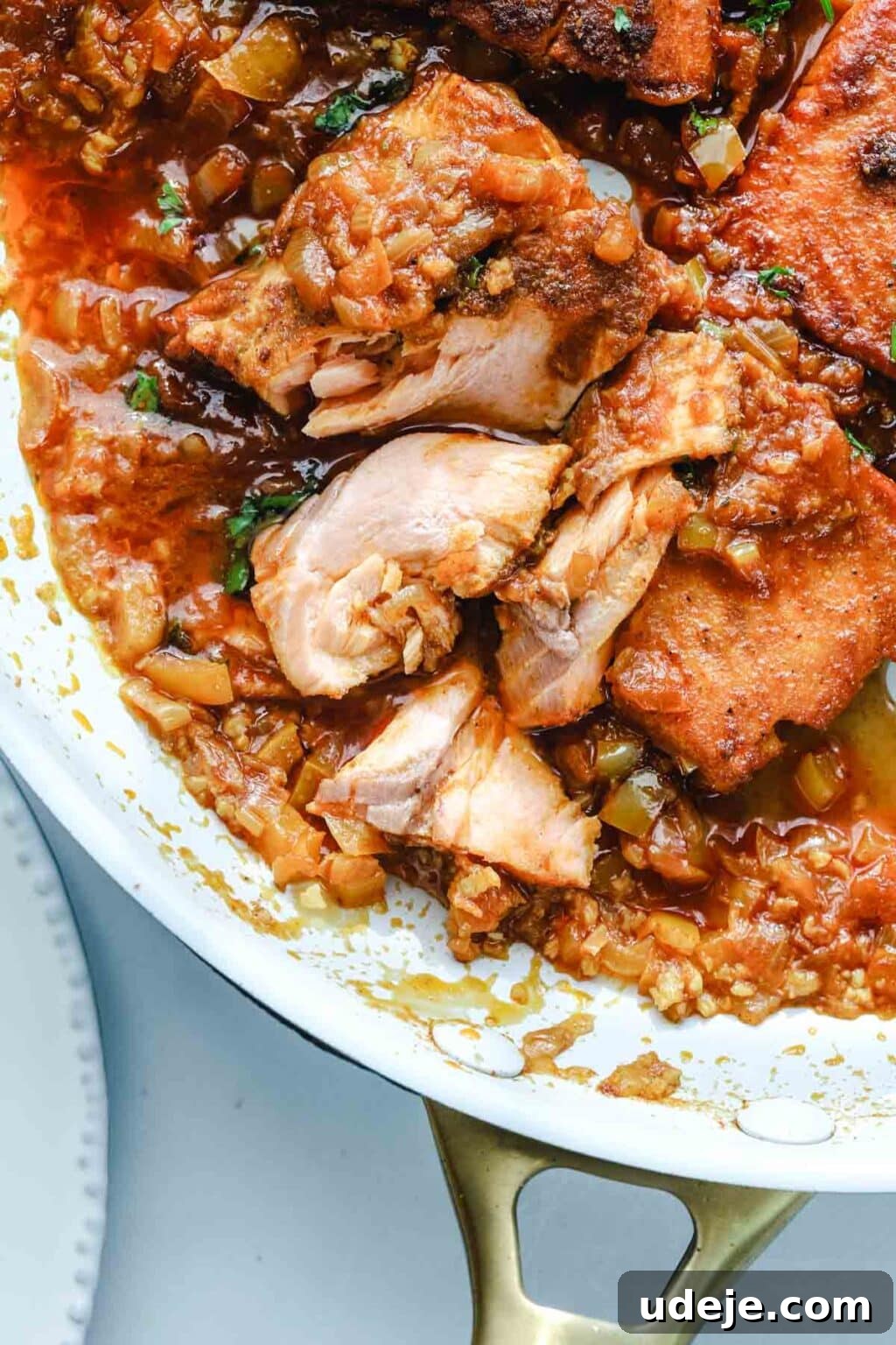 A light-colored skillet displays fish, cooked to perfection in a vibrant tomato sauce, artfully broken into flaky pieces, highlighting its tenderness and rich flavor.