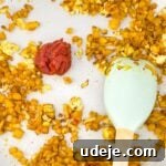 A light-colored skillet filled with beautifully cooked onions and vibrant yellow peppers, mingling with rich tomato paste, as a white spatula gently stirs the aromatic mixture.