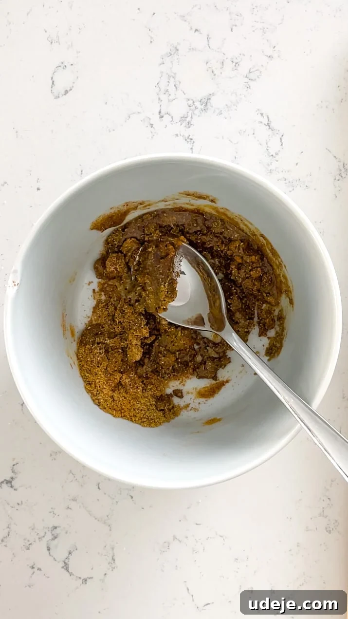 A small white bowl containing a vibrant, golden spice mix, with a spoon resting inside, ready for marination on a light-colored background.
