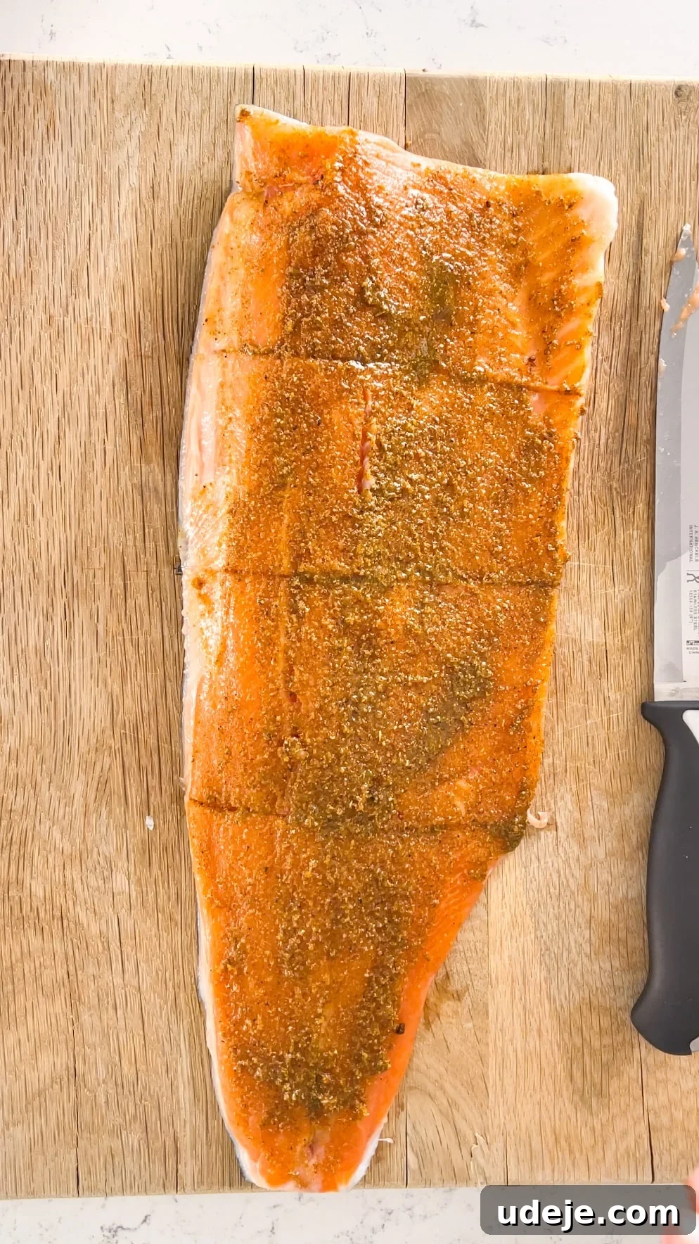 A glistening rainbow trout fillet, richly coated in an aromatic marinade, rests on a wooden cutting board, with a knife nearby, signaling it's ready for the next step of cooking.
