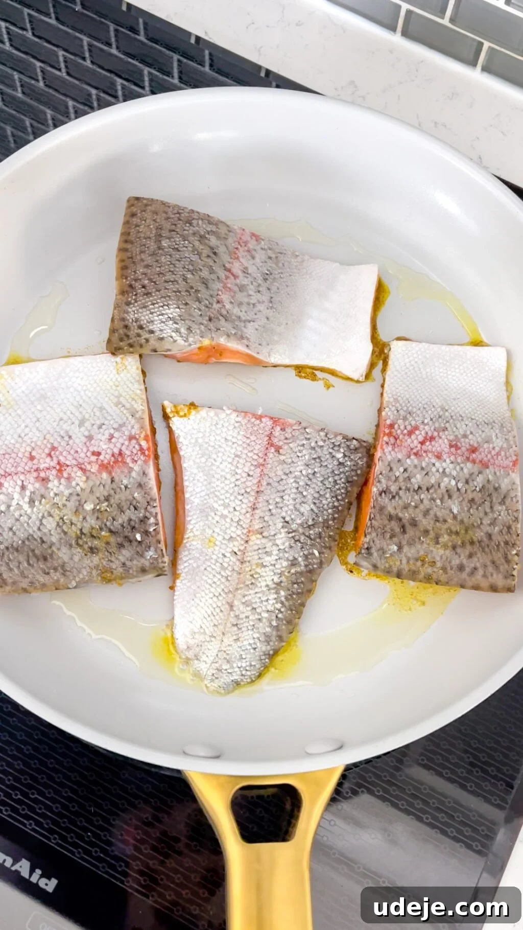 A light-colored skillet holds several pieces of fish, skin-side up, showing a slight crispness from a quick sear.