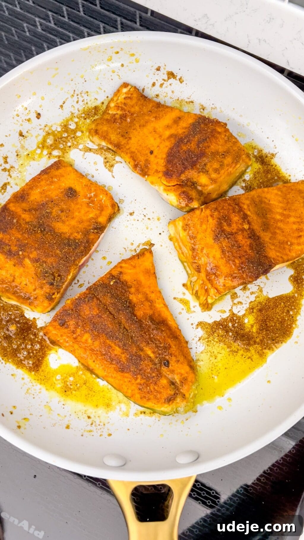 A light-colored skillet with pieces of fish that have been perfectly seared to a golden-brown, ready for the next step in the cooking process.