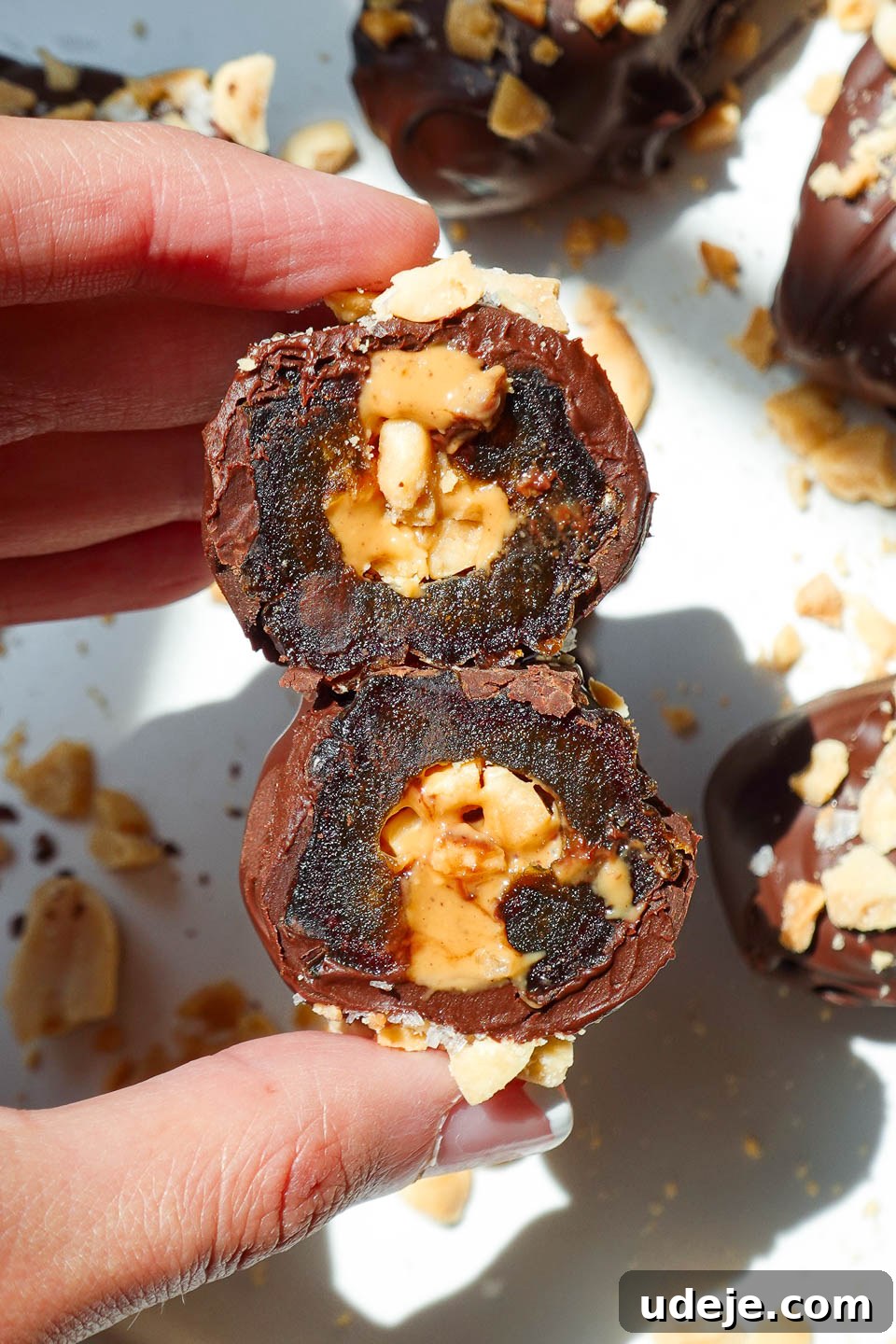 Snickers Date Bombs 2 Hand holding a Snickers Stuffed Date with a bite taken out to show the caramel-like texture of the Medjool date and creamy peanut butter filling.