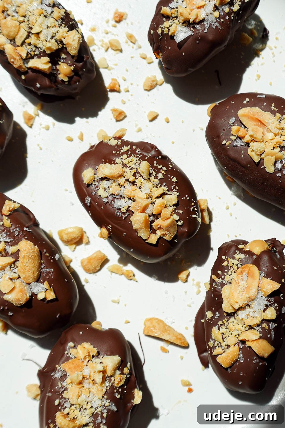 Snickers Date Bombs 3 Overhead shot of Snickers Stuffed Dates on a parchment-lined tray, dipped in chocolate and sprinkled with chopped peanuts, ready to be chilled.