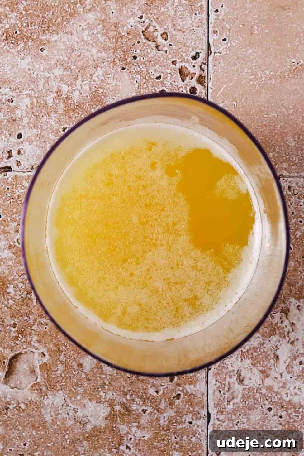Melted butter in a beige-colored bowl on a light stone tiled background, with separated milk solids.