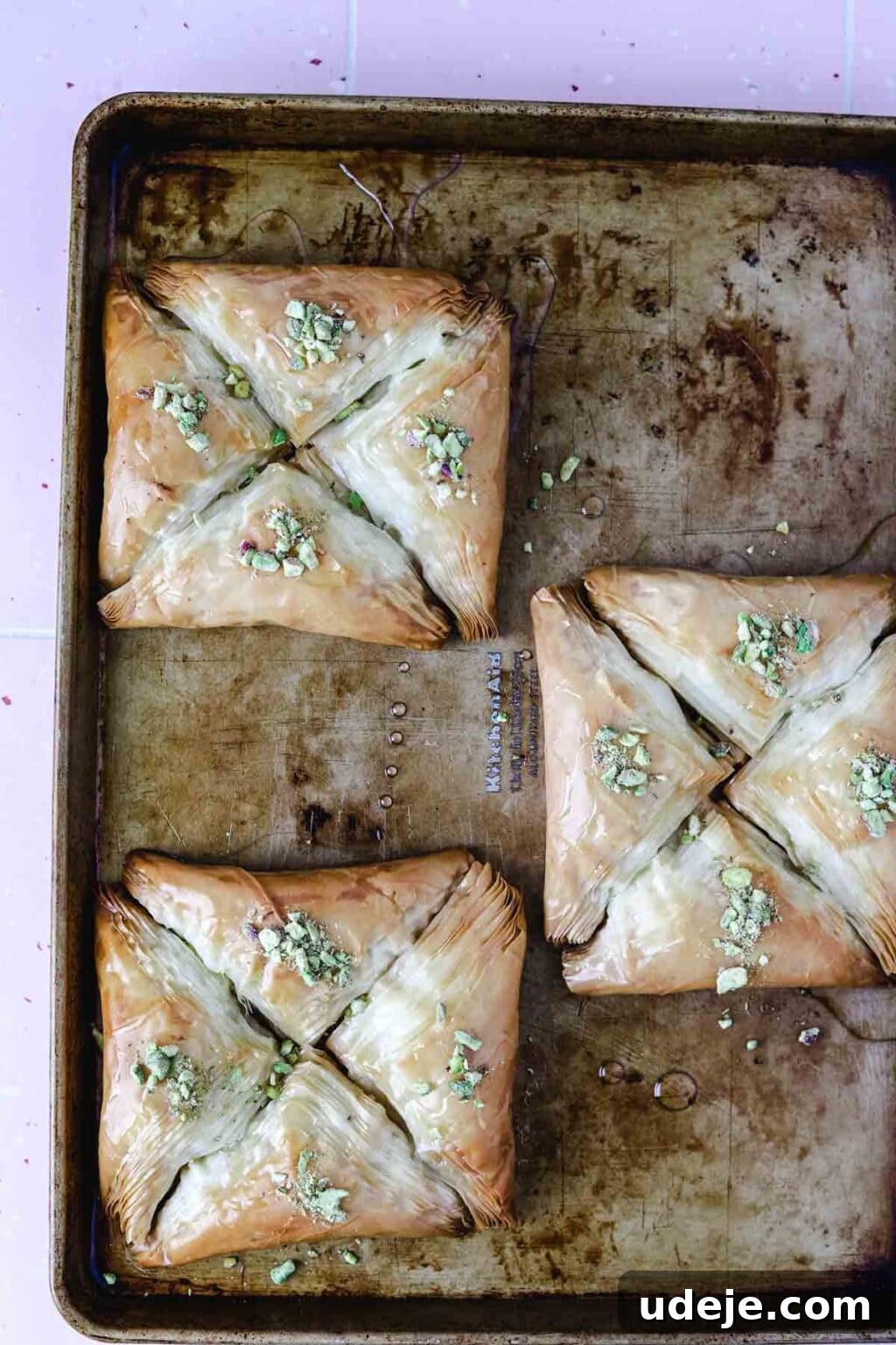 Three squares, each made of four triangular Warbat pieces, on a baking sheet after being baked and garnished with crushed pistachios.