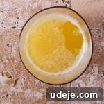 Melted butter in a beige-colored bowl on a light stone tiled background, with separated milk solids.