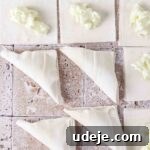 Pieces of square-cut phyllo with ashta in the middle, with four of them already folded into triangles, all on a light stone tiled background.