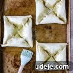 Three squares, each made of four triangular Warbat pieces, on a baking sheet, brushed thoroughly with butter using a silicone brush, on a light stone tiled background.