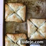 Three squares, each made of four triangular Warbat pieces, on a baking sheet after being baked, with a small pitcher of sugar syrup nearby.