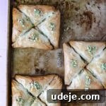 Three squares, each made of four triangular Warbat pieces, on a baking sheet after being baked and garnished with crushed pistachios.