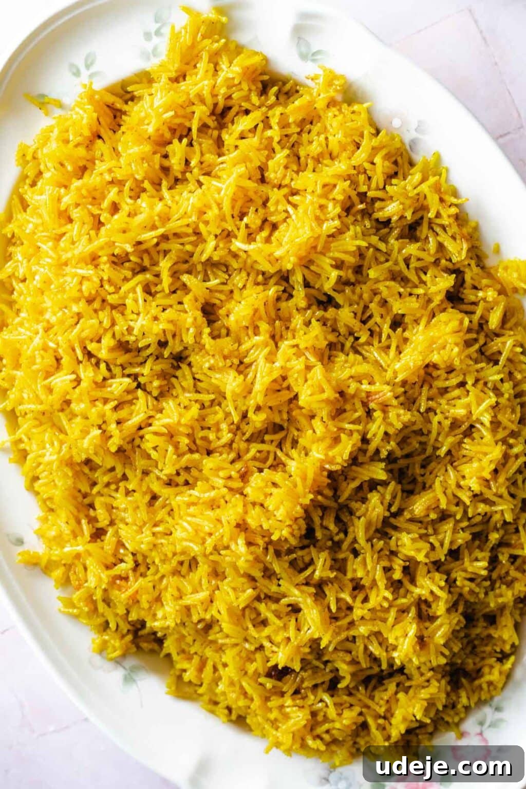 30-Minute Golden Mediterranean Basmati 8 A large, pristine white platter elegantly displays bright yellow Middle Eastern Rice. Each individual grain is distinct and glistens softly, a testament to its perfect cooking and the warm, inviting color imparted by turmeric. The rice is loosely piled, showcasing its fluffy texture and readiness to be served as a flavorful accompaniment. The simplicity of the plating highlights the natural beauty and appeal of the dish.