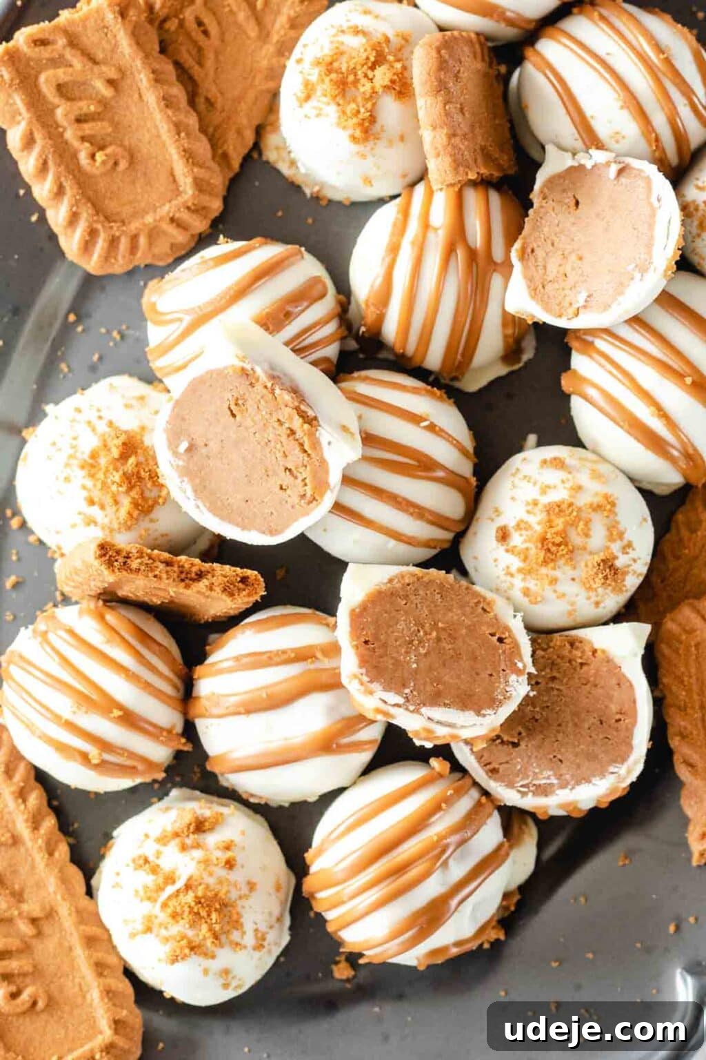 4-Ingredient No-Bake Biscoff Truffles 15 A stunning display of Biscoff truffles, some whole and some cut in half to reveal their creamy interior, arranged on a gray oval plate alongside whole Biscoff cookies, highlighting their deliciousness.