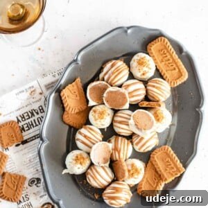 4-Ingredient No-Bake Biscoff Truffles 16 Biscoff truffles on a gray oval plate on a newspaper sheet with amber coloured glasses on a white marble background